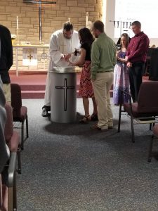 a minister and two people holding a baby for a baptism